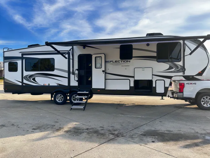 White Reflection Grand Design 5th wheel RV rental hitched to a 4x4 pickup, awning extended, ready for camping.. Grand Design Reflection 2022