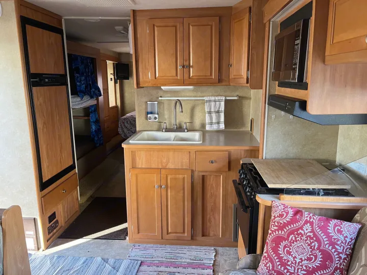 RV rental kitchen area features a sink, stove, microwave, fridge, and bunk beds are visible in the background.. Winnebago Access 2008