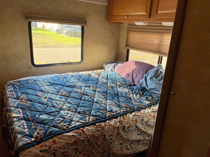 Cozy RV rental bedroom with a blue patterned quilt and scenic views from the windows.. Winnebago Access 2008