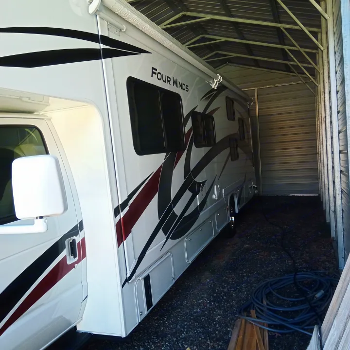 White Four Winds RV rental parked inside a large metal garage. This motorhome features black and maroon graphics.. Thor Four Winds 2022