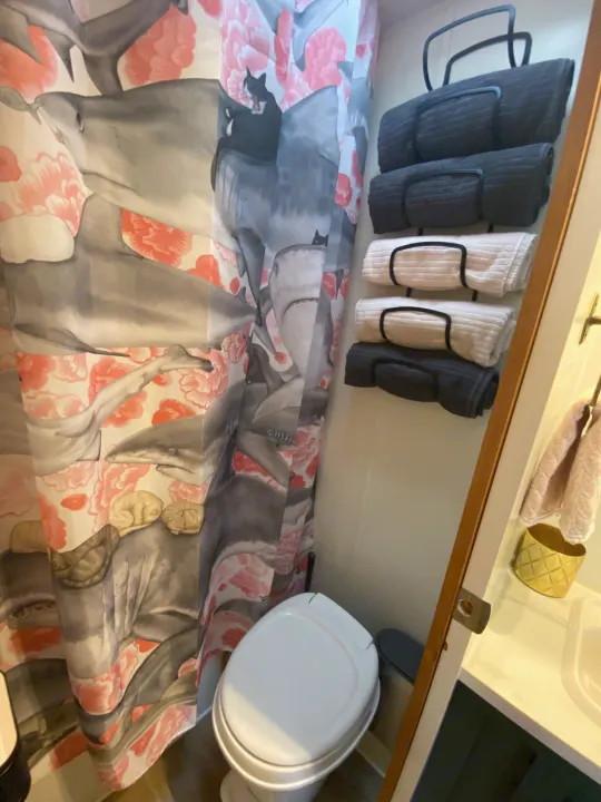 RV rental bathroom featuring a unique shark and cat shower curtain, white toilet, and neatly organized towels.. Jayco Jay Flight 2007