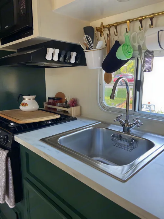 Inside an RV rental kitchen: dark green cabinets, white countertop, stainless steel sink, stove, and neatly arranged kitchenware.. Jayco Jay Flight 2007