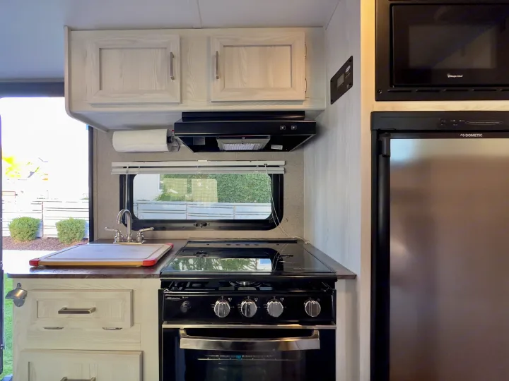 RV rental kitchen: light wood cabinets, Magic Chef microwave, Dometic fridge, Suburban stove, sink, and cutting board.. Forest River Rockwood GeoPro 2019
