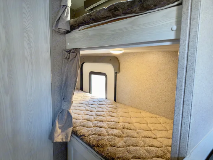 Interior of an RV rental showing cozy bunk beds with plush bedding, soft lighting, and a window.. Forest River Rockwood GeoPro 2019