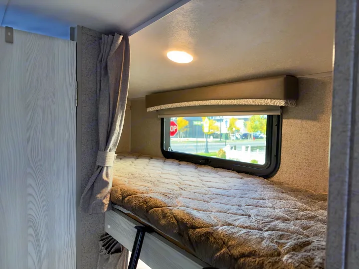 This RV rental features a cozy bunk bed with a soft comforter, window, and overhead light. Ideal for family travel.. Forest River Rockwood GeoPro 2019