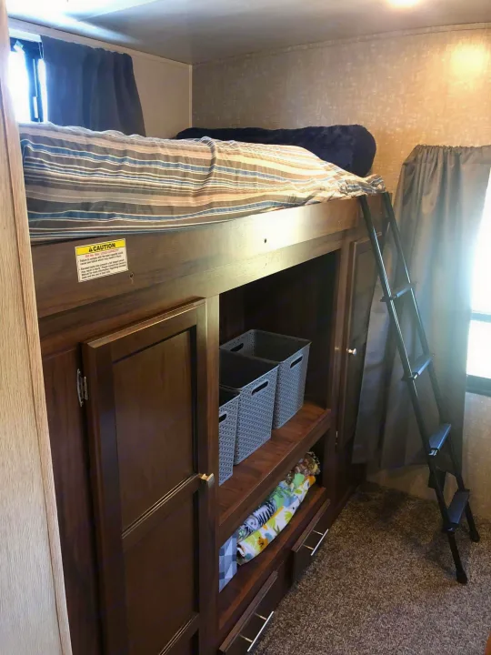 Cozy RV rental interior with a bunk bed, storage cabinets, and a ladder, ideal for travel accommodations.. Heartland RVs Mallard 2019