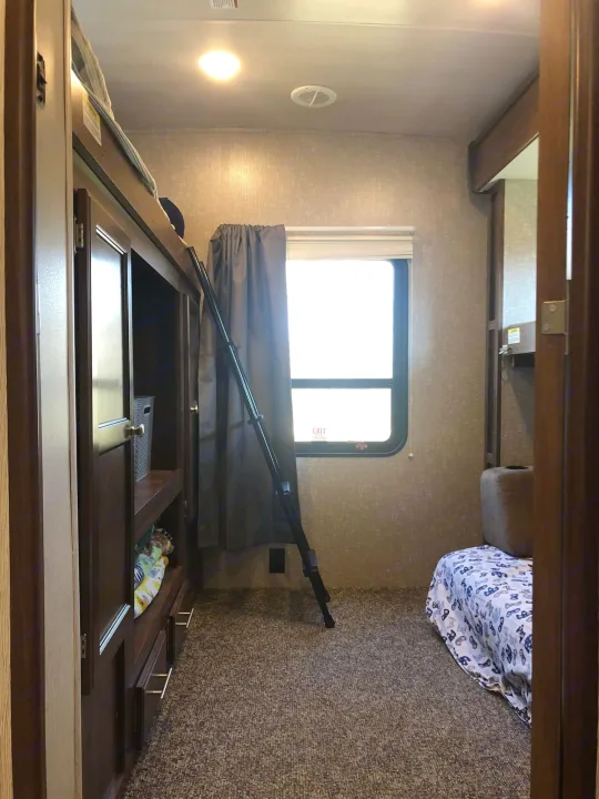 View inside an RV rental bunkhouse: dark wooden bunk beds, cabinet storage, a window, and a bed with patterned cover.. Heartland RVs Mallard 2019