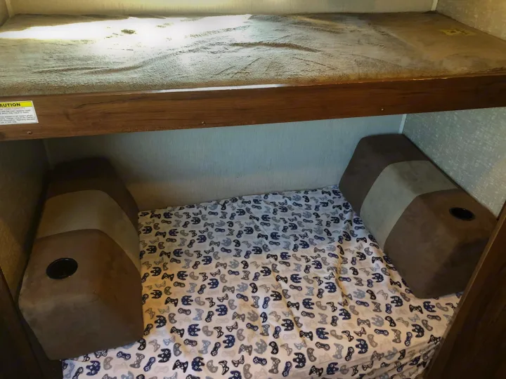 Cozy RV rental bunk beds: lower bed features fun gaming sheets & cup holders, while the upper bunk displays a caution sticker.. Heartland RVs Mallard 2019