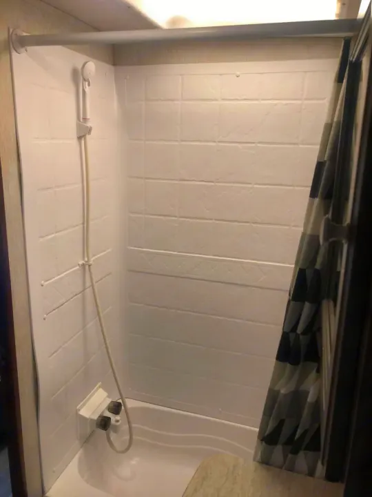 Compact shower/tub in an RV rental, featuring a hand-held showerhead and white molded walls. Ideal for travel.. Heartland RVs Mallard 2019