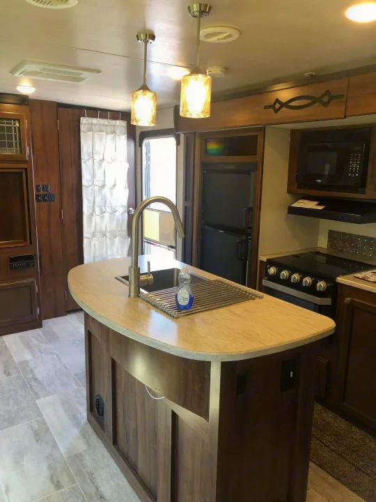 Well-appointed RV rental kitchen and living area, featuring an island, sink, stove, and microwave, perfect for compact travel.. Heartland RVs Mallard 2019