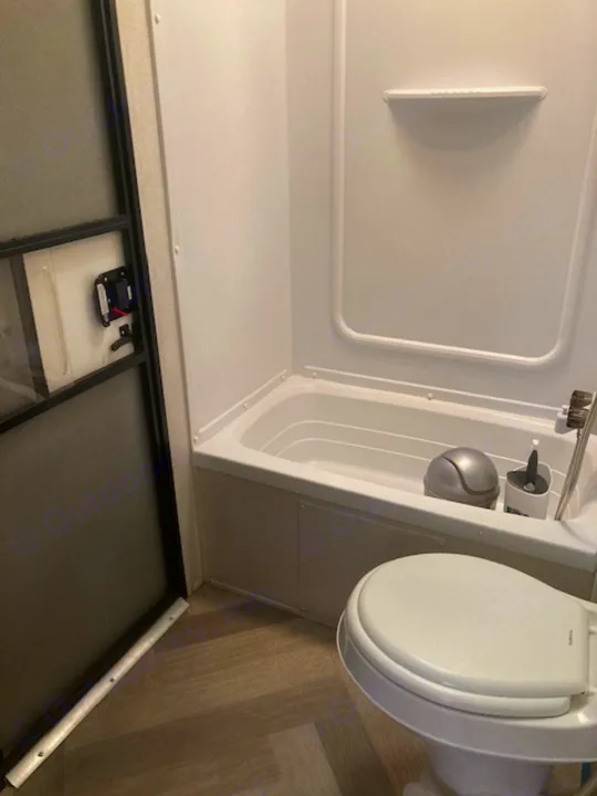 RV rental's compact bathroom shows a white shower, toilet, and stylish herringbone floor. Includes a functional folding door.. Forest River Salem 2020