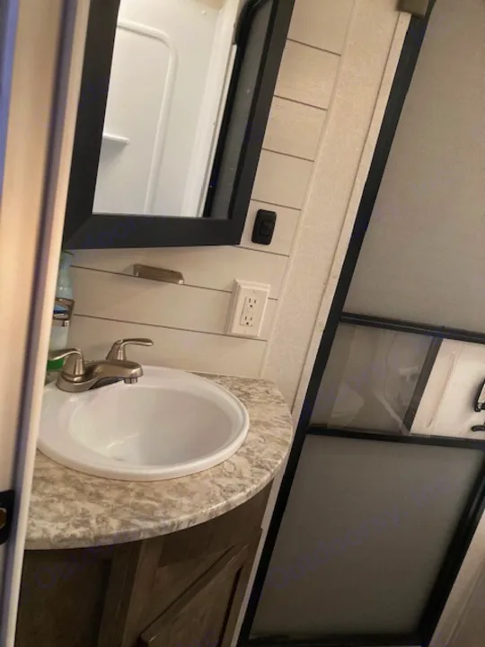 RV rental bathroom interior: A white sink in a speckled counter, with a power outlet nearby, and a dark-framed shower enclosure.. Forest River Salem 2020