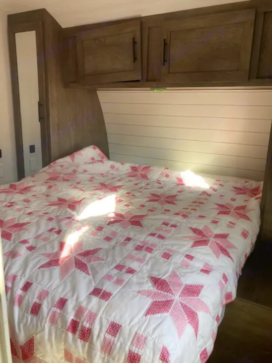 Compact RV rental bedroom showcasing a pink star quilt, wood storage, and white shiplap walls.. Forest River Salem 2020