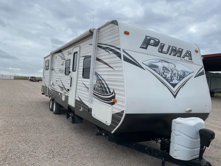White Puma travel trailer, a spacious RV rental, parked on a gravel lot under a cloudy sky, ready for your next adventure.. Palomino Puma 2015