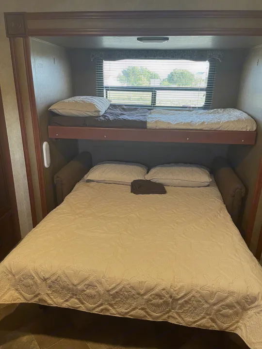 RV rental interior features a pull-out bed with a seashell-quilted cover and an upper bunk bed for travel.. Palomino Puma 2015