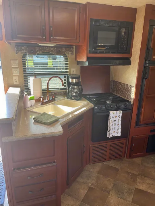 Well-equipped RV rental kitchen featuring dark wood cabinets, microwave, stove, double sink, and coffee maker.. Palomino Puma 2015