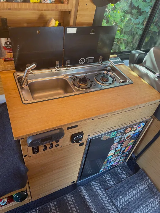 RV rental bamboo kitchen with integrated Dometic sink/stove, Redarc controls, and a refrigerator, ideal for travel.. Ford Transit Custom 2019