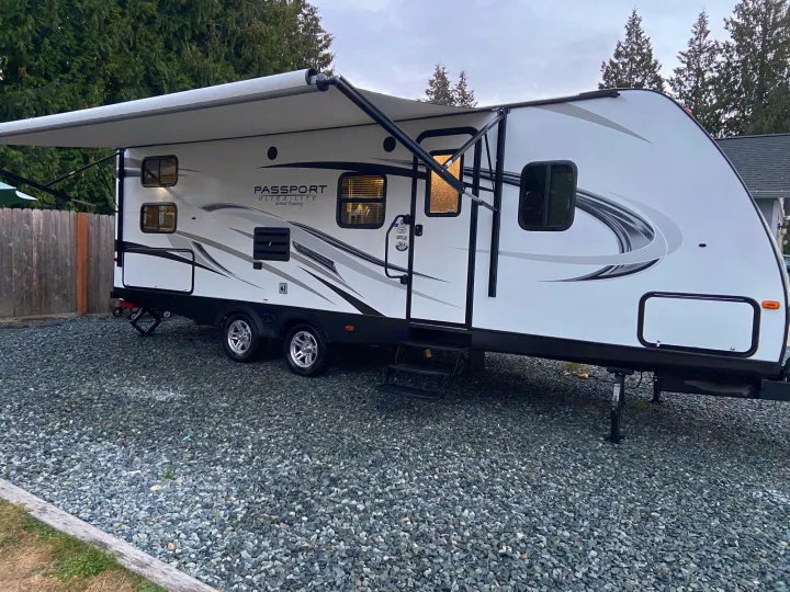 Explore the outdoors with this clean white travel trailer RV rental. Parked on gravel with the awning extended, ready for adventure.. Keystone Passport 2017