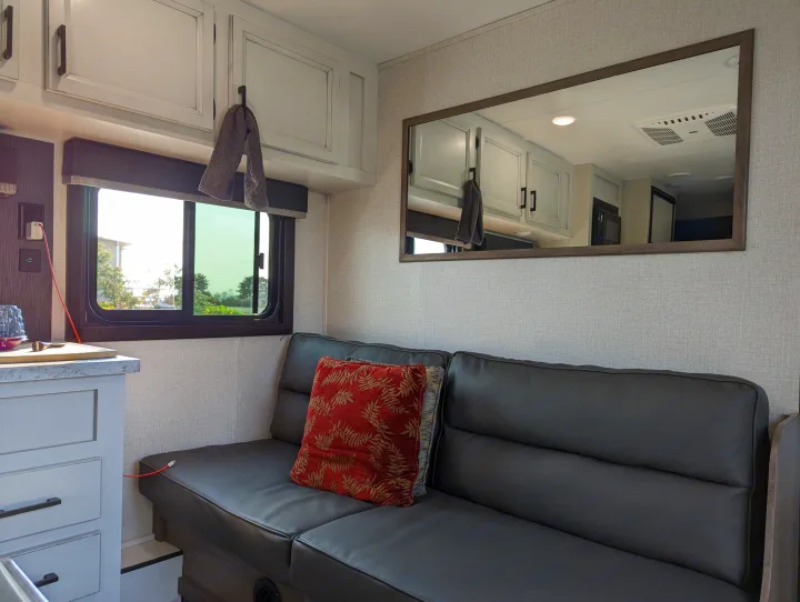 Inside this RV rental, a comfy sofa, overhead storage, and mirror reflecting the kitchen area create a cozy living space.. Highland Ridge RV Open Range 2022