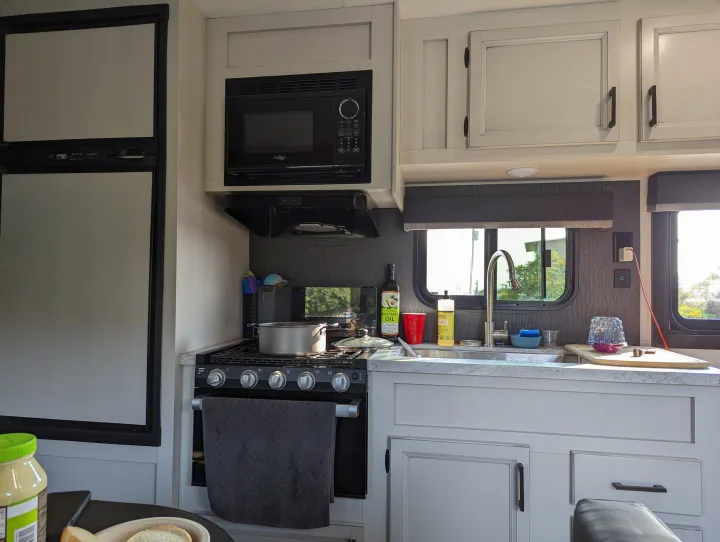Compact rv rental kitchen with microwave, stove, sink, and fridge, ready for meals on the go.. Highland Ridge RV Open Range 2022