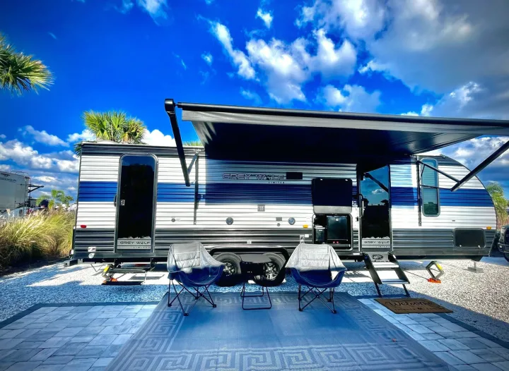 Grey Wolf travel trailer rv rental at a sunny campsite. Awning extended, outdoor mat, pavers, and chairs offer relaxation.. Forest River Cherokee Grey Wolf 2022
