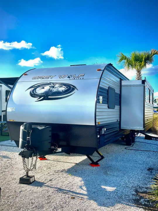 Modern Grey Wolf RV rental at a sunny campsite with a palm tree, its slide-out extended for extra space.. Forest River Cherokee Grey Wolf 2022