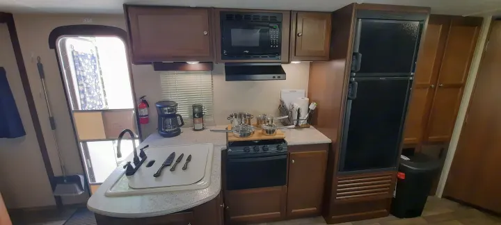 An RV rental kitchen view, showcasing a microwave, stove, sink with knives, and fridge for comfortable travel.. Keystone RV Bullet Ultra Lite 2016