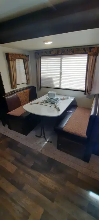 RV rental dinette: a cozy interior with brown upholstered benches, white table, and two windows with blinds.. Keystone RV Bullet Ultra Lite 2016