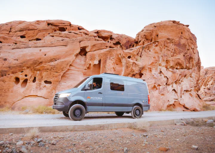 A grey Moterra camper van RV rental on a dirt road, parked by stunning red rock formations in a desert landscape.. Mercedes-Benz Sprinter 2020