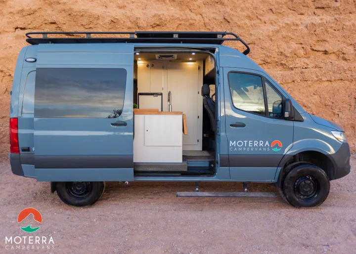 Moterra campervan RV rental parked on a dirt road, side door open revealing its custom interior kitchen. Ready for adventure.. Mercedes-Benz Sprinter 2021