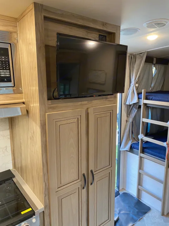 RV rental interior shows light wood cabinets, TV, microwave, and bunk beds. Modern, comfortable amenities for your trip.. Palomino Solaire Ultra Lite 2021