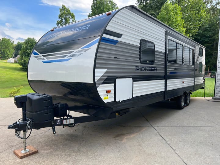 Modern Pioneer travel trailer, white and grey with blue accents, parked on concrete. Perfect for your next RV rental!. Heartland Pioneer 2021