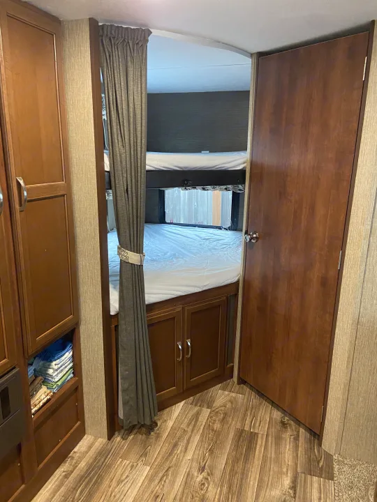 An inviting bunk room in an rv rental, featuring two beds, built-in storage, and durable wood-look flooring.. Keystone Passport 2017