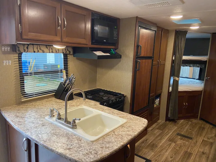 RV rental kitchen and living area, complete with a sink, stove, microwave, fridge, and adjacent bunk beds. Ready for your adventure.. Keystone Passport 2017