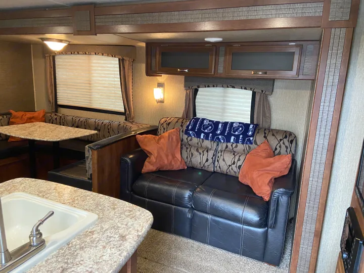 Explore this inviting RV rental interior: dining area, kitchen sink, and sofa with pillows. Your adventure awaits!. Keystone Passport 2017