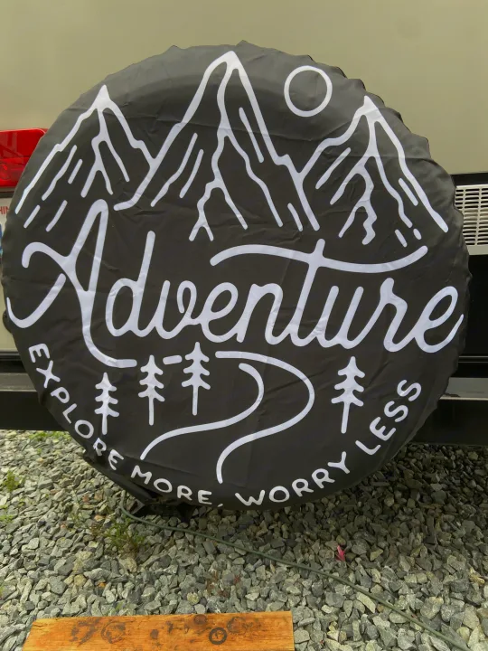 Adventure-themed spare tire cover for an RV rental, featuring mountains, sun, trees, and "Explore More, Worry Less" text.. Keystone Passport 2017