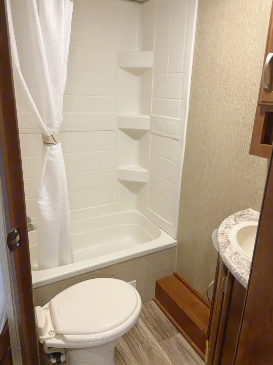 Step inside this RV rental's compact bathroom, showcasing a white shower/tub combo, toilet, and small sink vanity.. Keystone Passport 2017