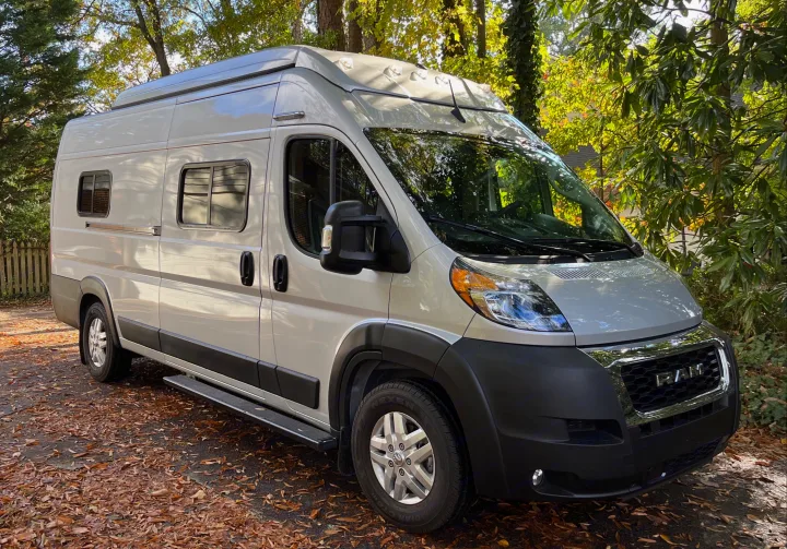 A light-colored Ram ProMaster camper van, an ideal RV rental, parked on a leafy autumn driveway with trees in the background.. Winnebago Solis PX 2023