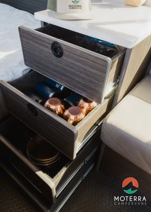 Efficient RV rental storage: three open drawers with kitchenware like copper mugs and plates in a campervan.. Mercedes-Benz Sprinter 2021