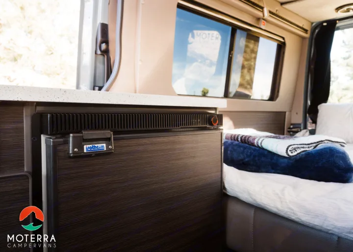Experience comfort in this Moterra rv rental: a built-in fridge, cozy bed, and countertop in a modern camper van interior.. Mercedes-Benz Sprinter 2021