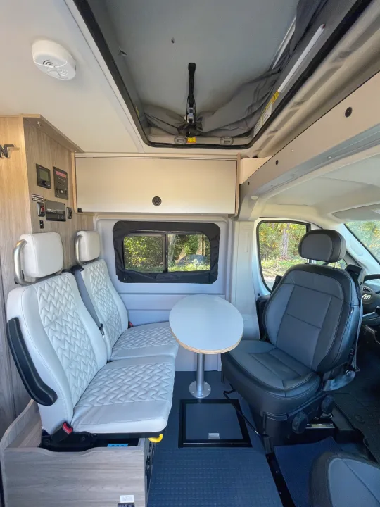 Spacious RV rental interior with quilted seats, table, control panel, and pop-top roof, ready for travel.. Winnebago Solis PX 2023
