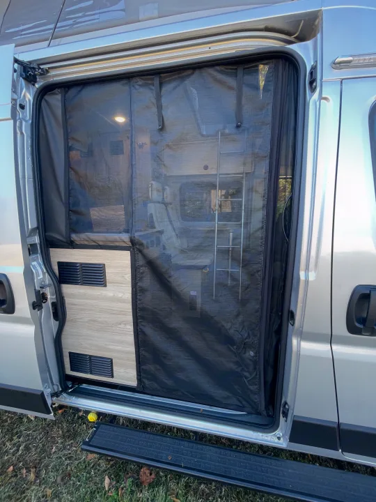 RV rental camper van side door open with an installed black mesh screen, offering ventilation and interior views.. Winnebago Solis PX 2023