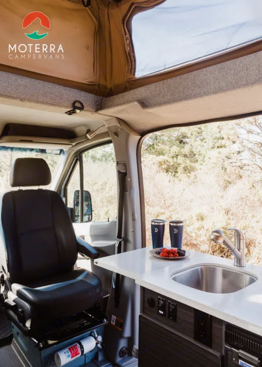 Inside a modern RV rental: Features a well-equipped kitchen area with a sink, comfortable front seat, and pop-top roof.. Mercedes-Benz Sprinter 2021