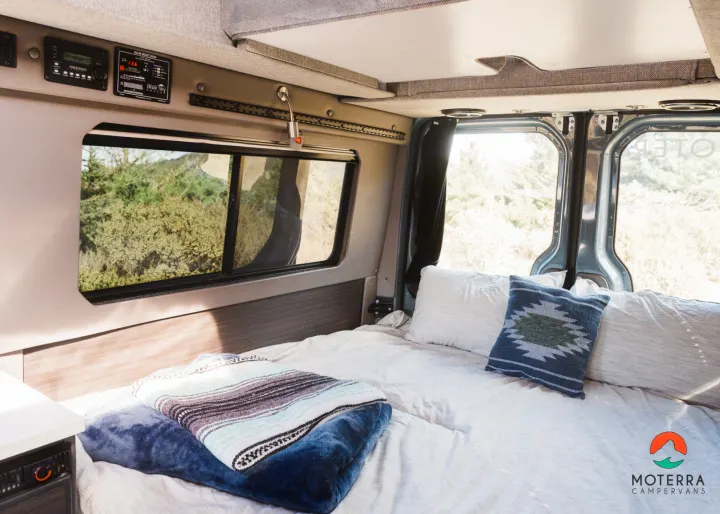 Cozy RV rental interior: a plush bed, control panel, and window with natural landscape views.. Mercedes-Benz Sprinter 2021