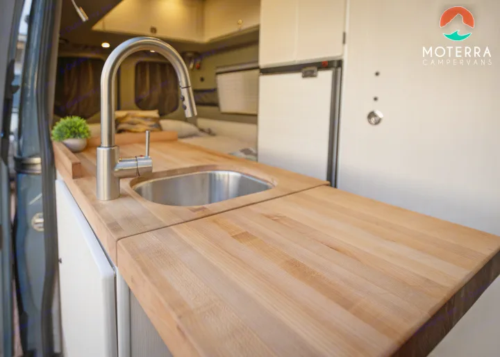 View of a compact RV rental kitchen featuring a light wood countertop, stainless steel sink, and modern faucet.. Mercedes-Benz Sprinter 2020