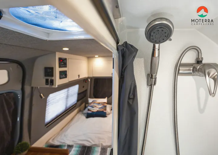 Inside a modern RV rental, featuring a sleek shower stall on the right and a comfortable bedroom with a bed & window beyond.. Mercedes-Benz Sprinter 2020