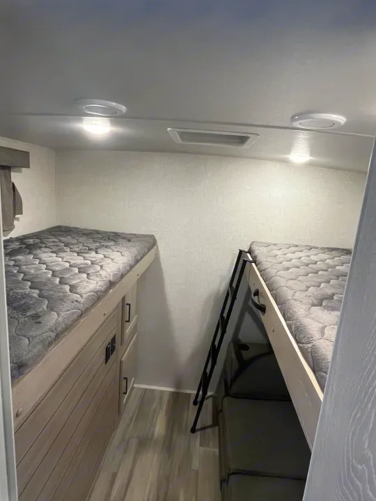 Cozy rv rental bunk bed area: two comfy mattresses, lower bed with storage, upper with ladder, and ceiling lights.. Forest River Rockwood Ultra Lite 2021