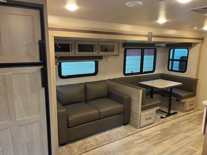 Modern RV rental interior with a gray sofa, U-shaped dinette, and refrigerator. Light wood accents perfect for your adventure.. Forest River Rockwood Ultra Lite 2021