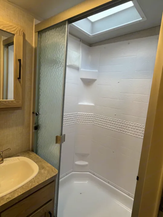 Modern RV rental bathroom showcasing a vanity, sink, and spacious shower with textured glass door, built-in shelves, and skylight.. Forest River Rockwood Ultra Lite 2021
