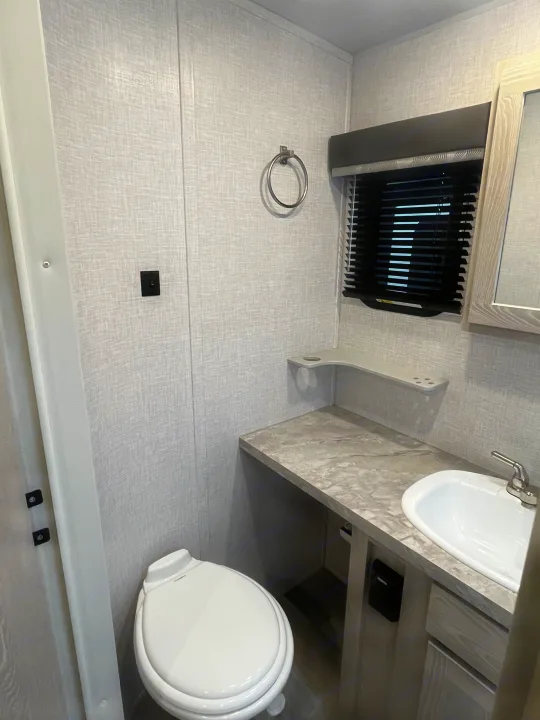 Inside an RV rental: a compact bathroom with a toilet, sink vanity, and window. Light textured walls and a practical layout.. Forest River Rockwood Ultra Lite 2021